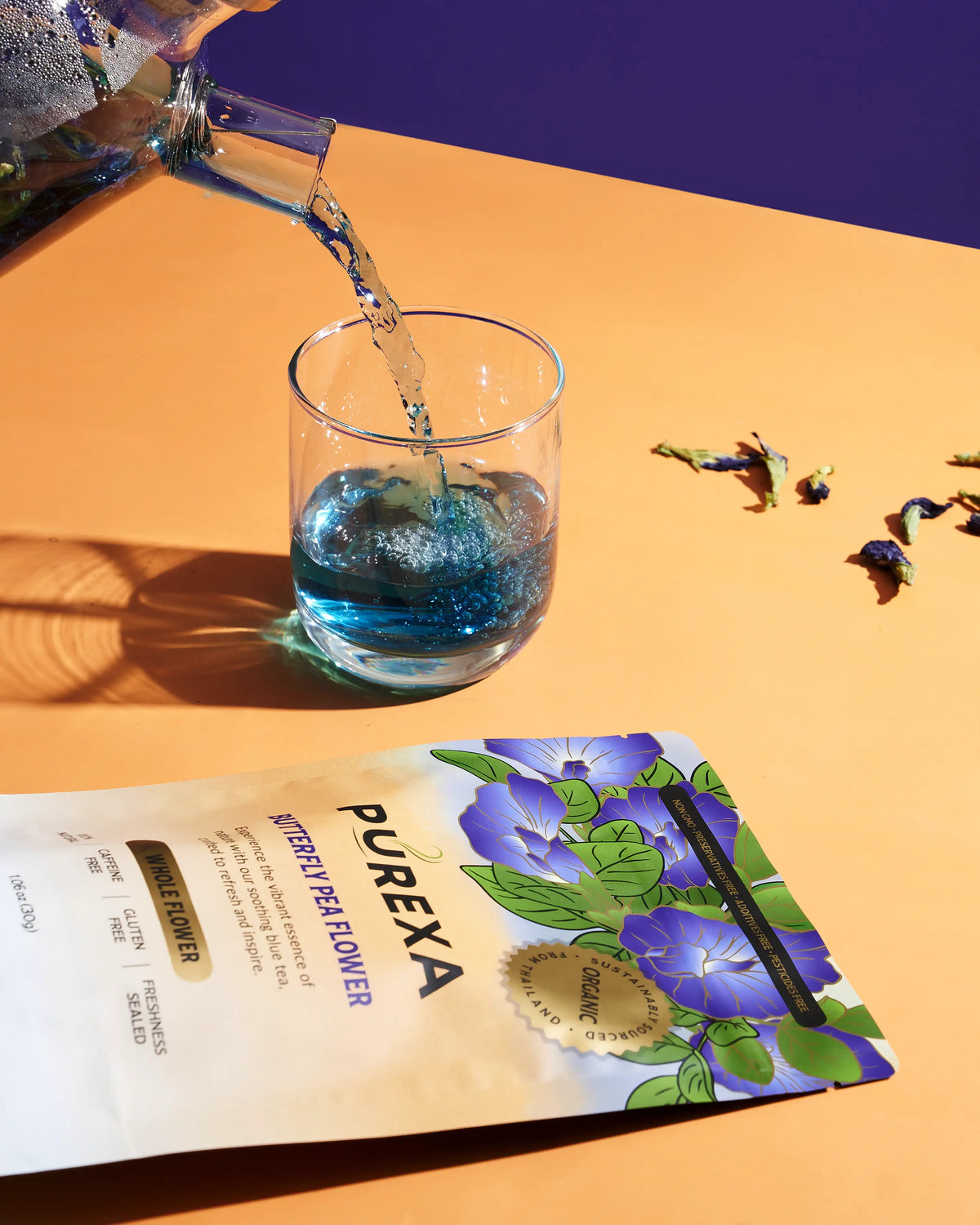 Blue butterfly pea tea being poured from a glass teapot into a cup