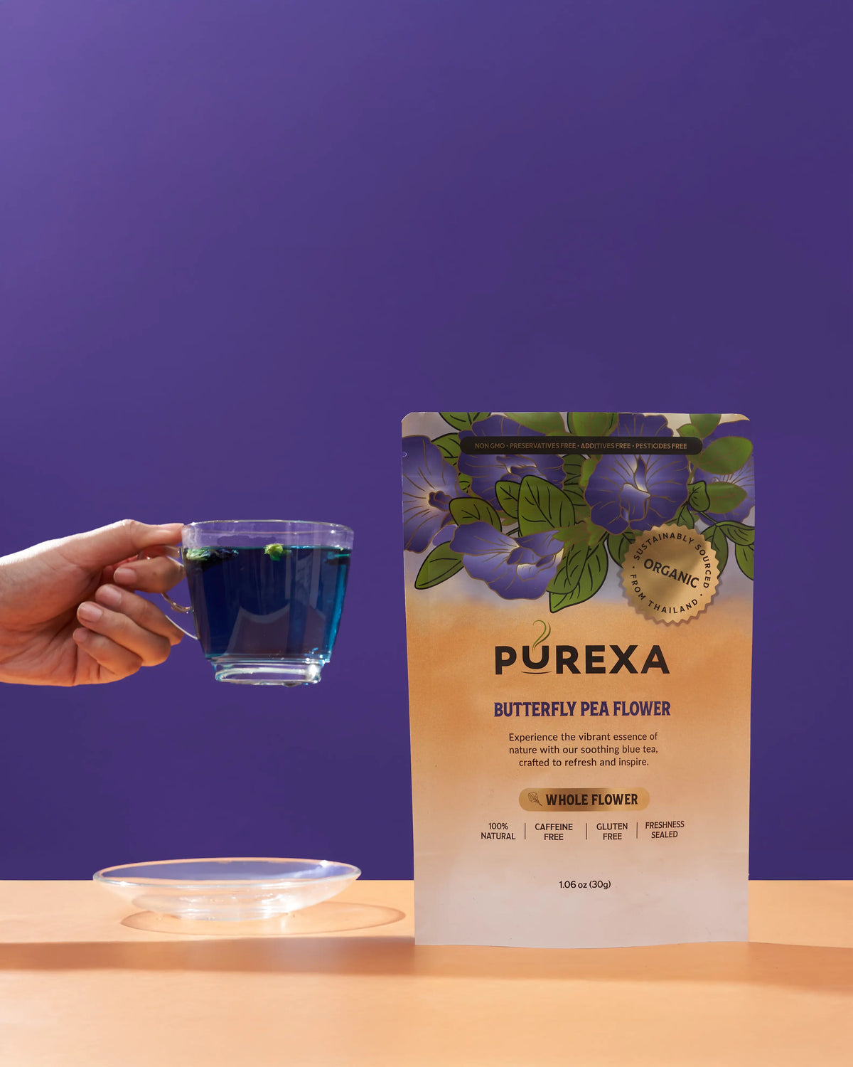 Glass cup of vivid blue butterfly pea tea beside PUREXA whole-flower pouch